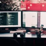 Deux écrans d’ordinateur affichant du code et une interface, sur un bureau avec clavier, souris et smartphone en charge. Création site e-commerce chalon-en-champagne.